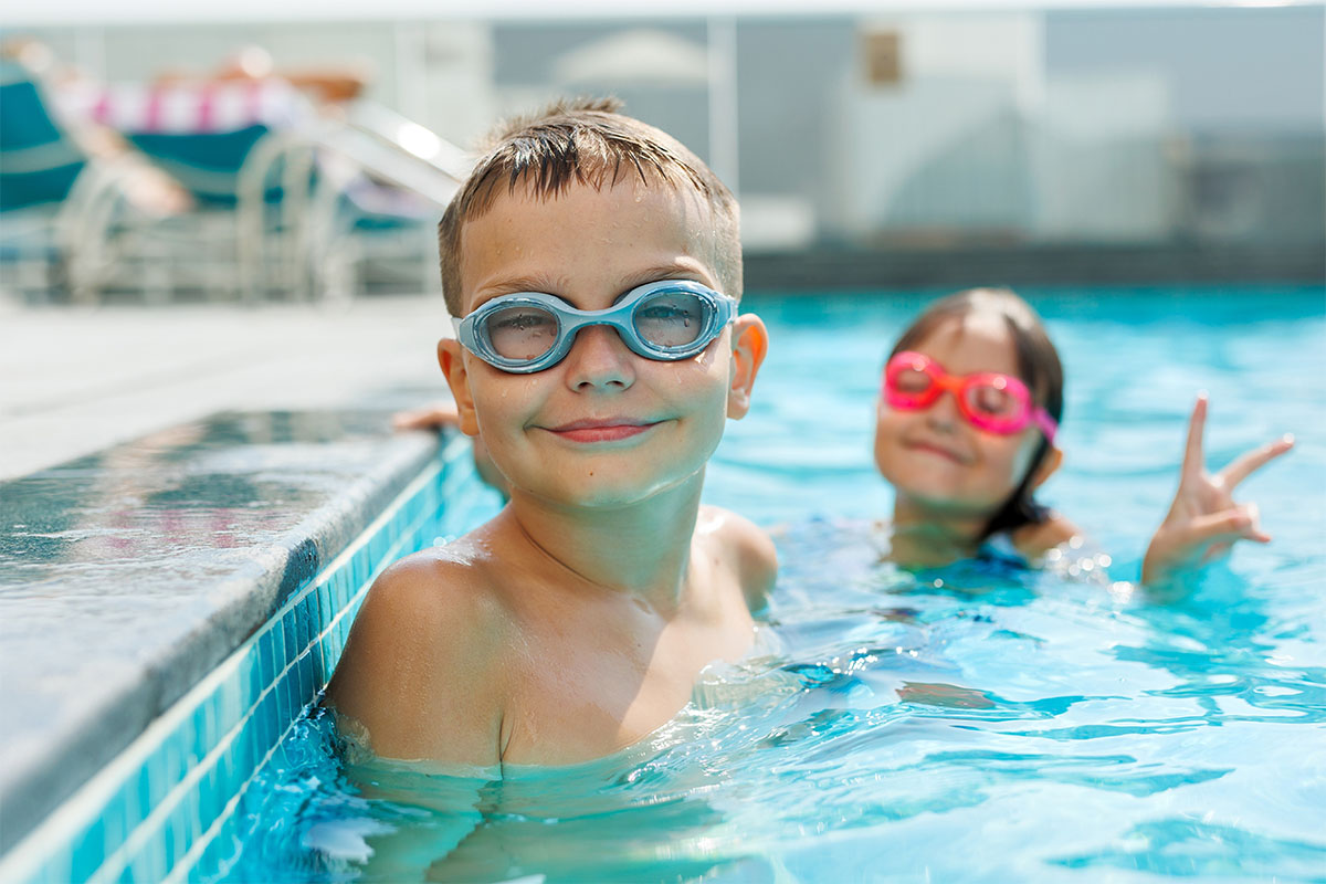 Bambini con occhialini da nuoto sorridono in una piscina durante una lezione di nuoto.
