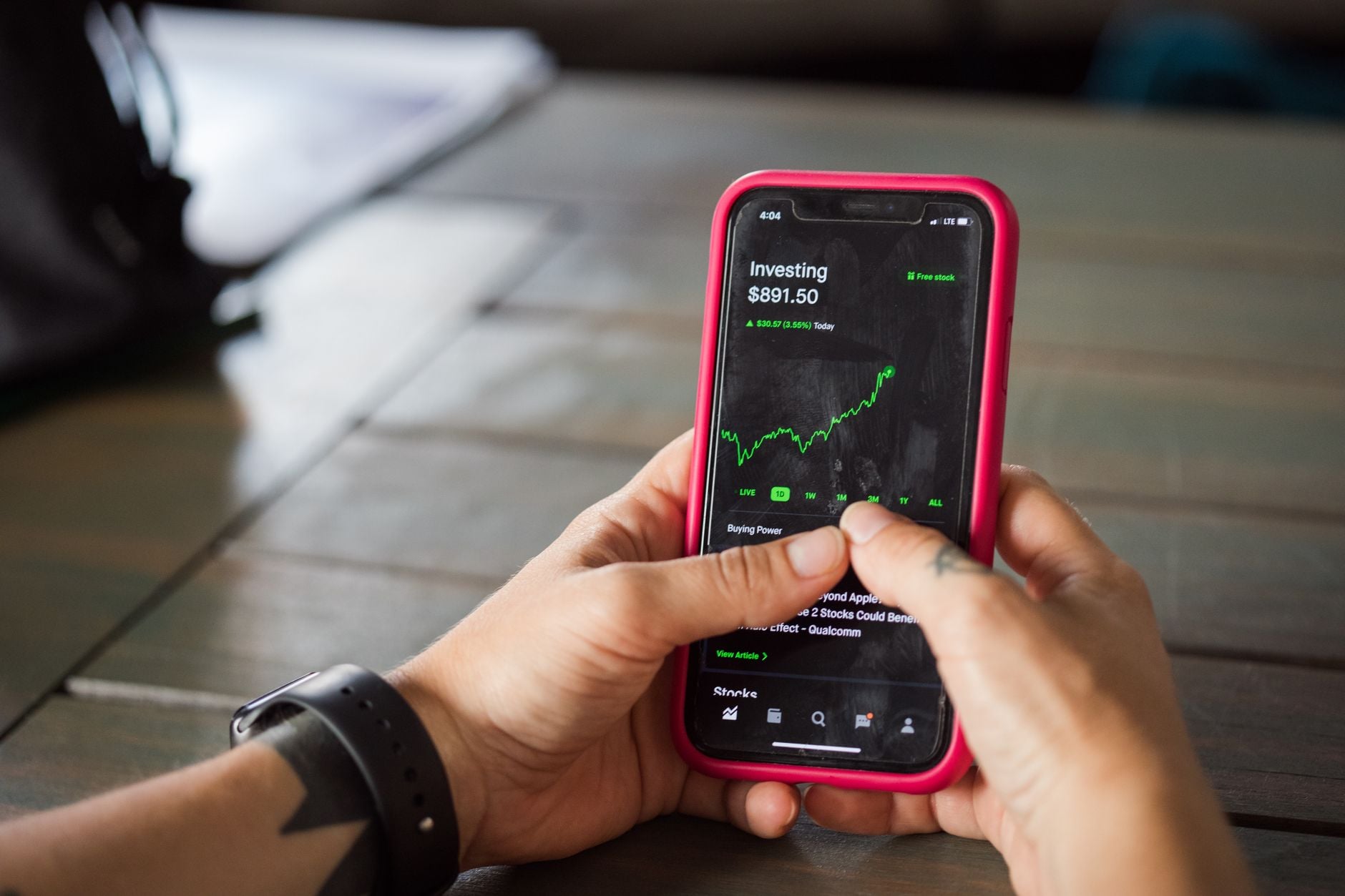 Person holding pink smartphone displaying investment portfolio with $891.50 and upward trending green stock chart