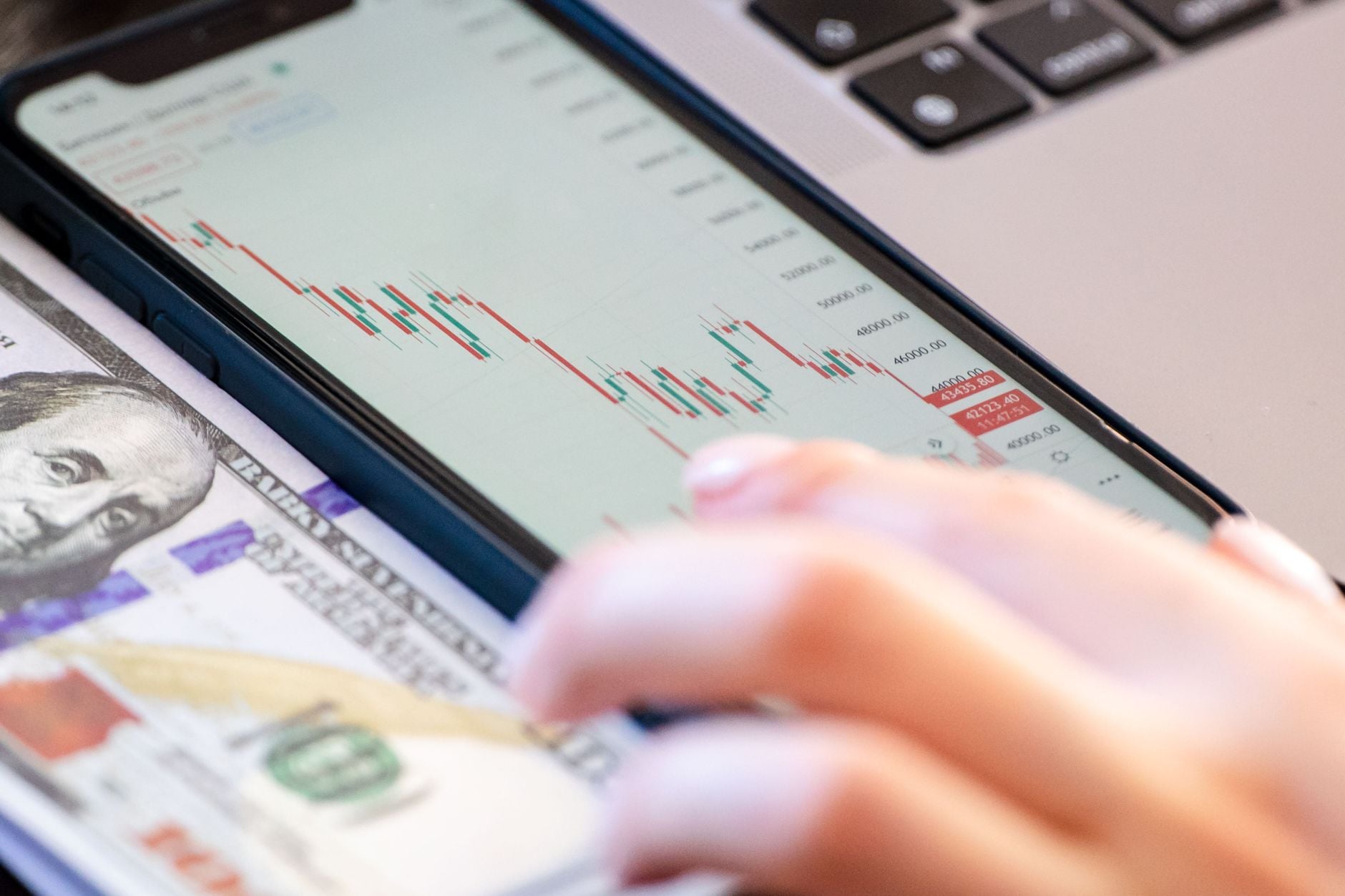 Tablet screen showing candlestick stock chart with red and green bars, hand pointing at financial data