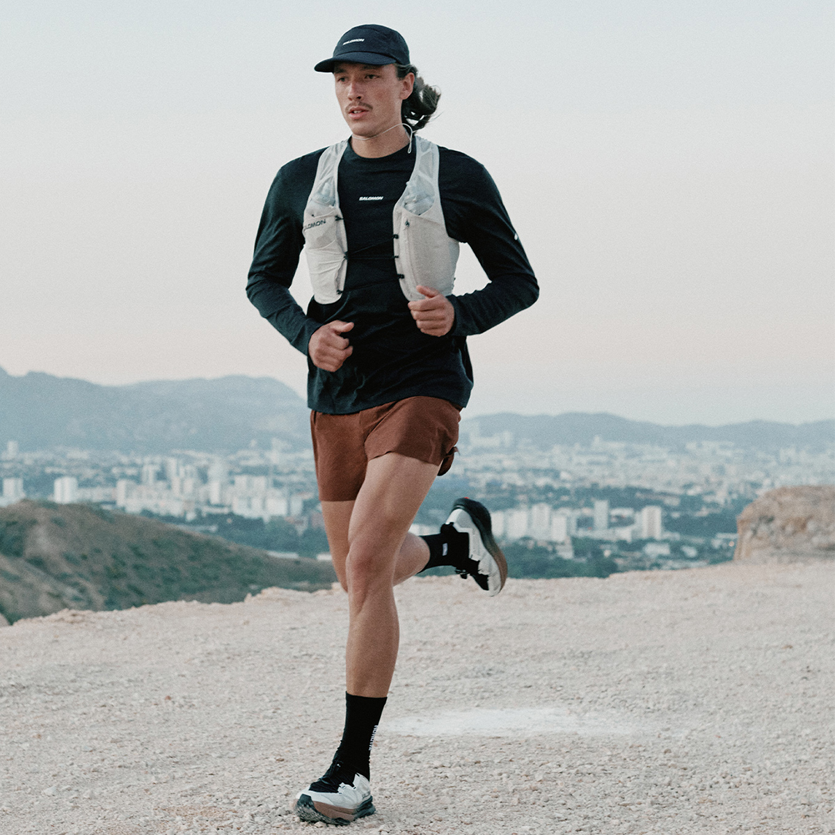 Corridore uomo in abbigliamento sportivo corre su una strada sterrata con vista panoramica della città.