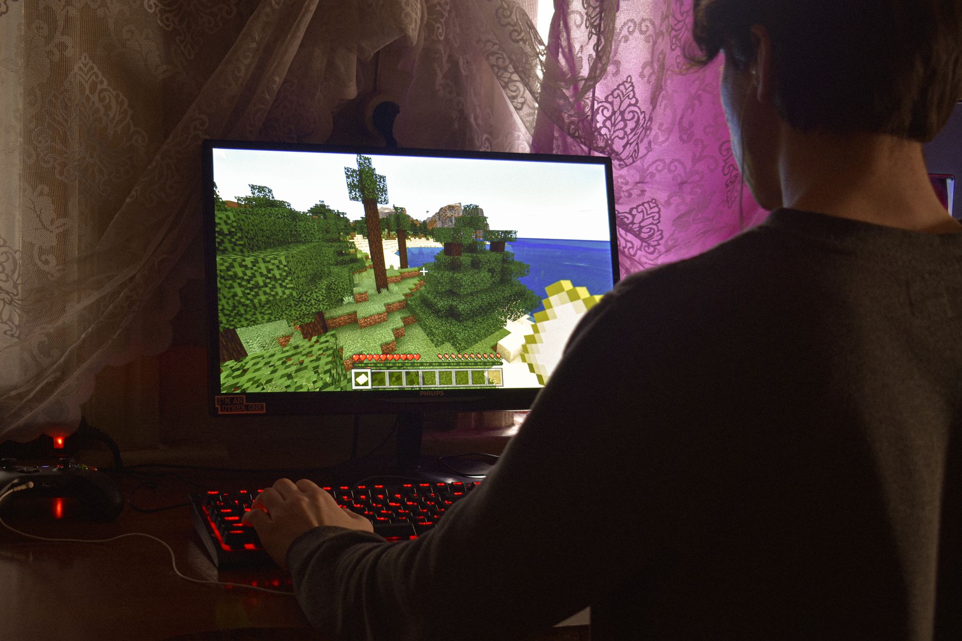 Player sitting at desk with red mechanical keyboard, viewing Minecraft gameplay on monitor