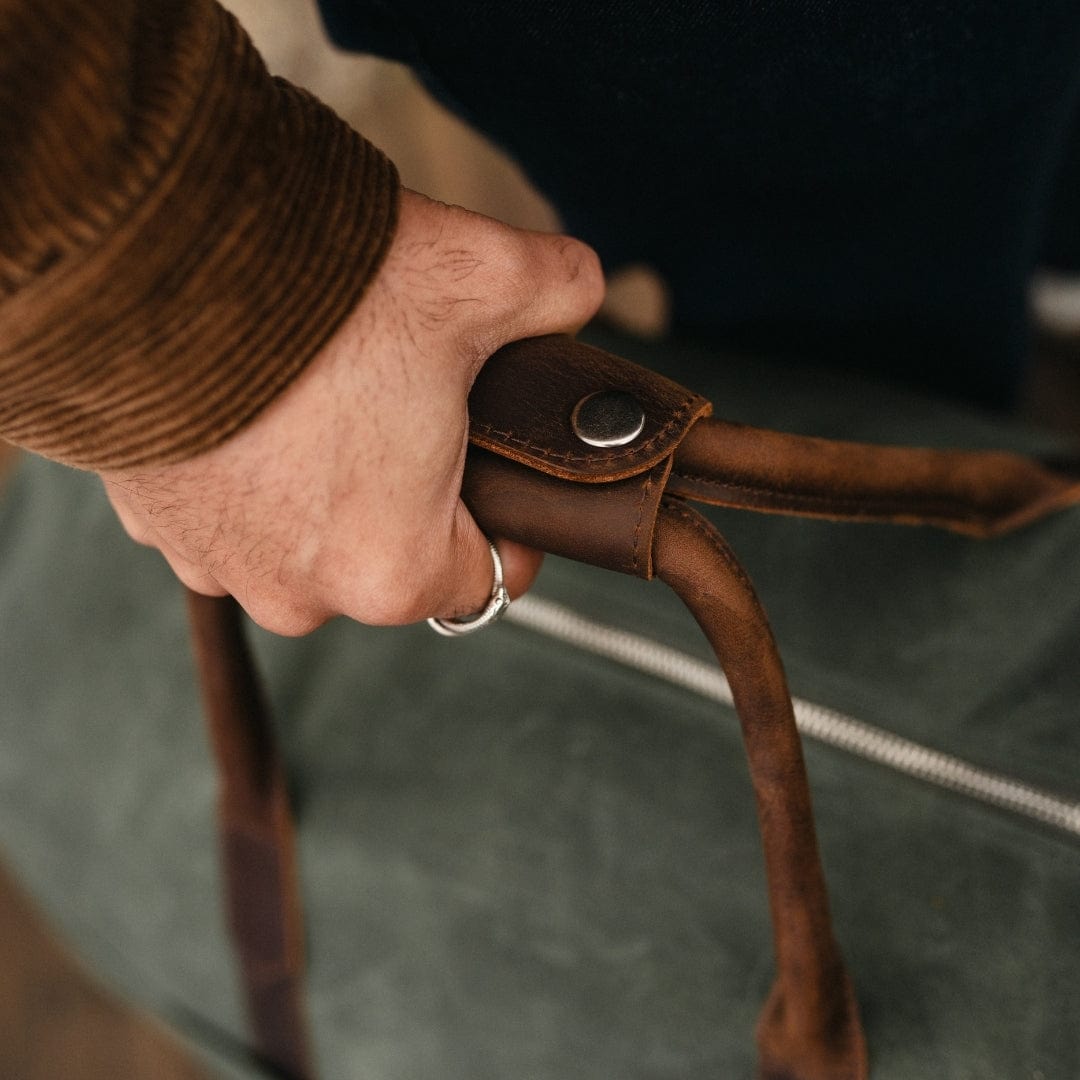 Closeup of brown leather bag handle with metal snap detail and rope cord